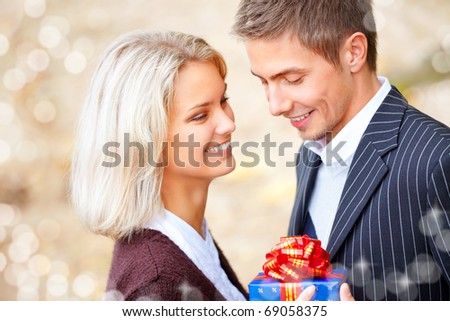 Happy young couple in love with a gift-box. They are laughing and embracing. Blurry lights on a foreground.