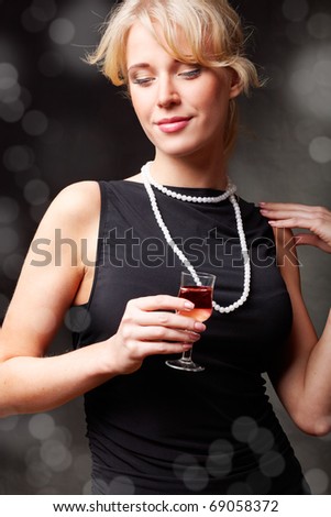 Portrait of a sexy girl in evening dress holding a glass of wine. On dark background with blurry lights.