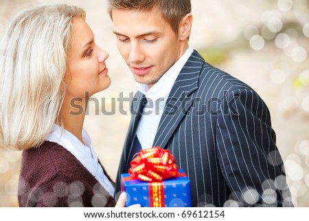 Happy young couple in love with a gift-box. They are laughing and embracing. Blurry lights on a foreground.