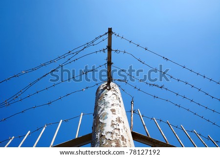 Barbed wire against clear blue sky. With part of metal fence.