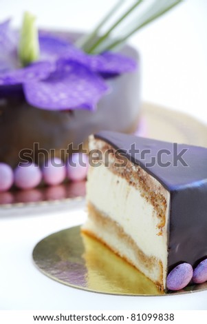 Piece of tiramisu cake with chocolate frosting. Uncut cake in the background.