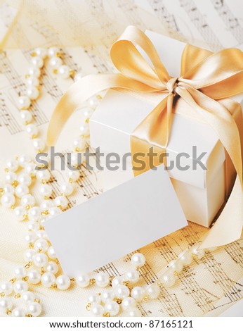 Gift box tied with gold ribbon with gift card and pearl necklace on musical notes.