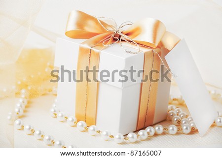 Gift box tied with gold ribbon with gift card and pearl necklace.