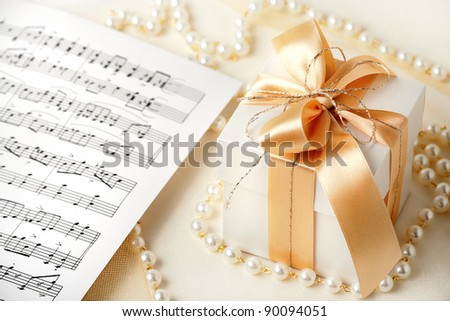 Gift box  tied with gold ribbon and sheets of musical notes and pearl necklace.
