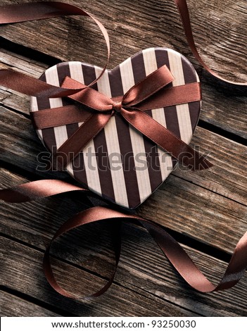 Heart shaped Valentines Day gift box with curved ribbon on old wood. Vintage holiday background.
