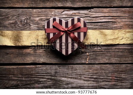 Heart shaped Valentines Day gift box with wrinkled golden ribbon on old wood. Vintage holiday background.