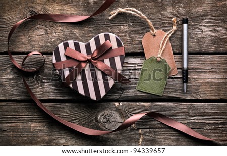 Heart shaped Valentines Day gift box with blank gift tag and fountain pen on old wooden background.