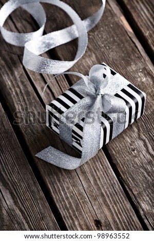 Gift box tied big silver bow with curved silver ribbon on old wooden background.