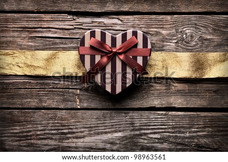 Heart shaped gift box with golden ribbon on old wood. Vintage holiday background.