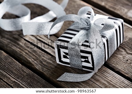 Gift box tied big silver bow with curved silver ribbon on old wooden background.