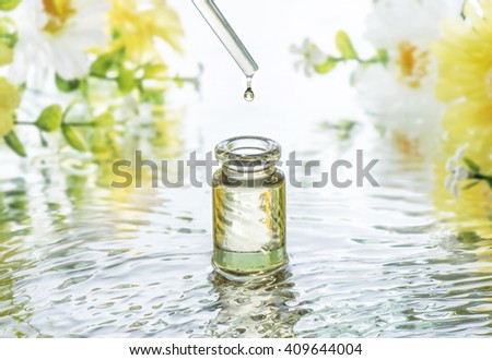 The bottle of Moisturizing cosmetic oil in the water waves on the  flowers blur background and pipette with oil drop above the bottle