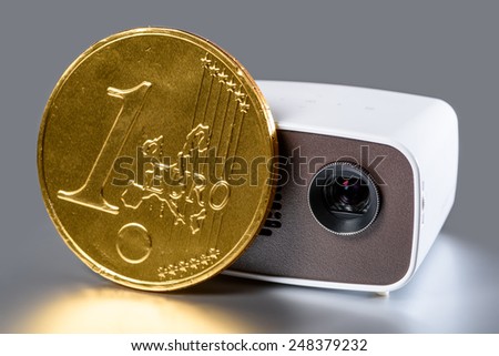 Mini Projector with golden euro coin for size comparison reflecting on a silver background