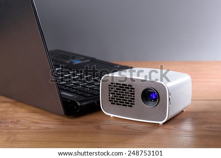 Battery operated mini projector with a laptop on a desk. The transfer of the image is wireless.