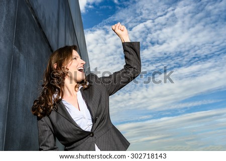 Young business woman in victory pose in front of the blue cloudy sky.