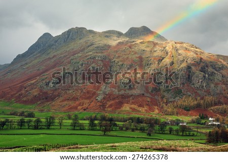 The last remnants of a rainbow and a shaft of sunlight enliven this moody shot of the towering Langdale Pikes.