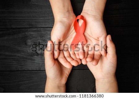 AID red ribbon in hand on a black wooden background, a symbol of the fight against HIV, AIDS and cancer. concept of helping those in need