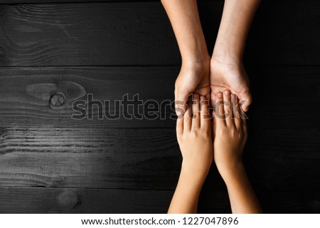 top view arms stretches out and holds one another on black wooden background. joint support and assistance in the community, children\'s hands help each other with support