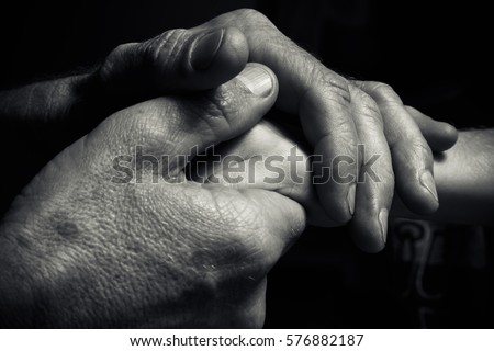 Hands of an elderly man holding the hand of a younger man. Lots of texture and character in the old man hands. black and white