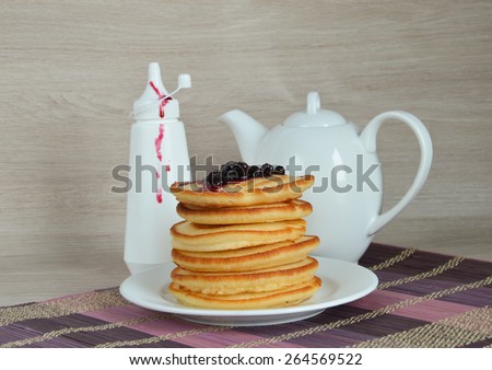 Fluffy pancakes with currant syrup, syrup bottle and teapot on wooden background