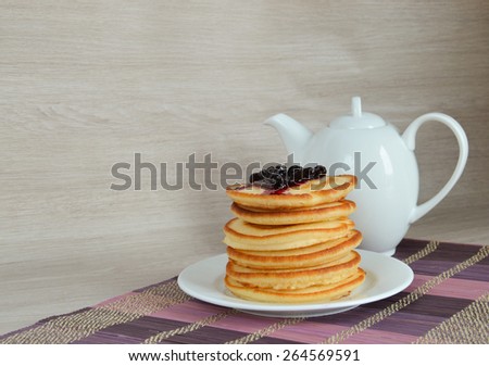 Fluffy pancakes with currant syrup and teapot on wooden background