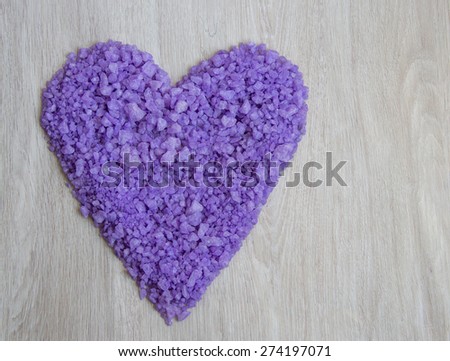 Heart-shaped purple bath salts on grey wooden background