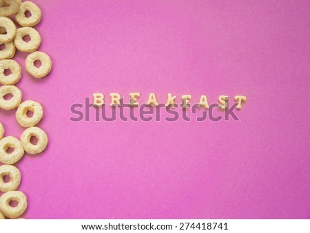 Word Breakfast Written With Pasta Letters on pink background with cereal rings