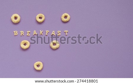 Word Breakfast Written With Pink Pasta Letters on violet background with cereal rings