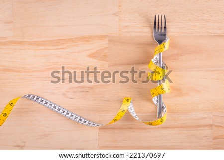 Knife and fork wrapped in tape measure on wooden table with copy space. Cutlery with tape. Symbol for diet and weight loss.