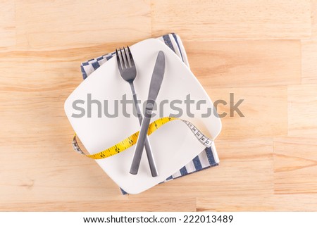 Empty plate with measure tape, knife and fork. Diet food on wooden table. Above view