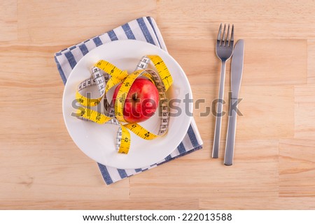 Red apple on plate with measure tape, knife and fork. Diet food on wooden table.  Above view