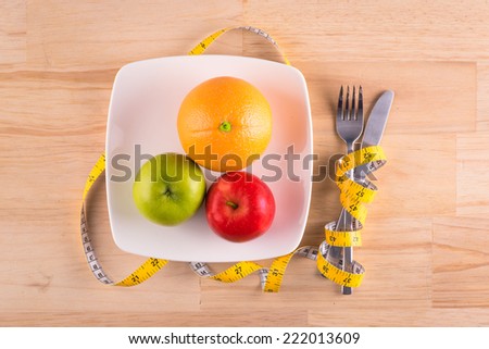 fruits in plate with measure tape, knife and fork. Diet food on wooden table
