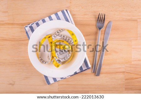 Empty plate with measure tape, knife and fork. Diet food on wooden table.  Above view