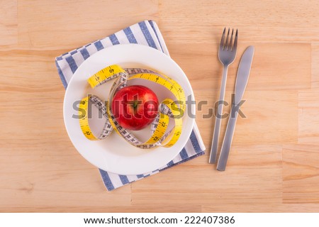 Apple on dish with measure tape, knife and fork. Diet food on wooden table.  Above view
