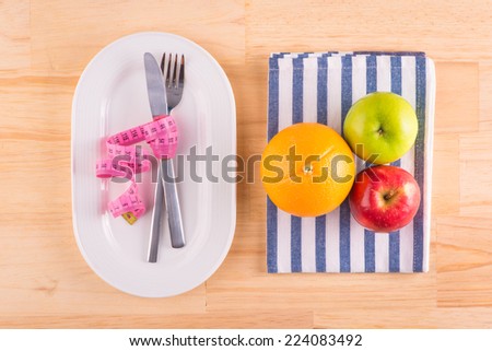 Diet concept. Fruits with measuring tape on a plate. measure tape with knife and fork - Diet food on wooden table with copy space