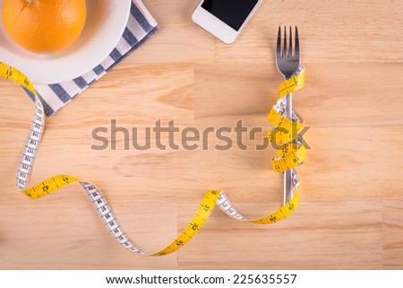 Plate with measure tape, cup, knife and fork. Diet food on wooden table