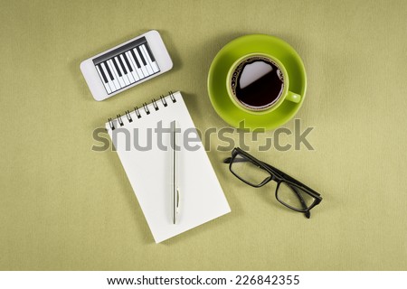 Mobile with blank paper or notebook and cup of coffee on green wooden desk. Simple workspace or coffee break with relaxing composing.