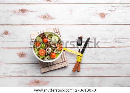 Fitness salad and measuring tape on rustic wooden table. Mixed greens, tomatos, diet cheese, olive oil and spices for healthy lifestyle concept.