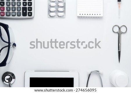 Modern medicine workplace with digital tablet, notepad, stethoscope, glasses, calculator, bottles, pills and syringes at doctor\'s desk. Copy space view from the top