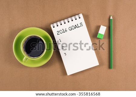 Office table with notebook, pencil and coffee cup. View from above with copy space. New year 2016 resolution. Open diary with 2016 goals words