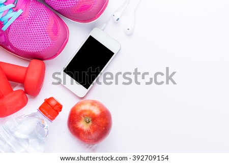 fitness concept with mobile phone, towel, shoes, dumbbells, red apple and woman sport footwear over white background. View from above