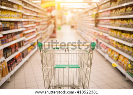 Supermarket aisle with empty red shopping cart with customer defocus background