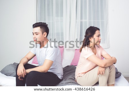 Young Unhappy Asian Couple Sitting Back To Back On Sofa At Home