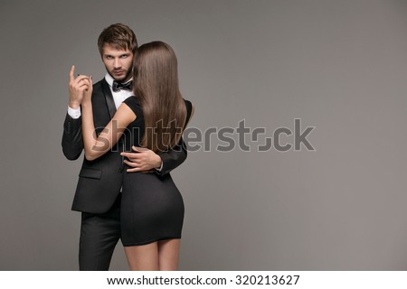 sexy man in a suit hugging a mysterious woman in a little black dress