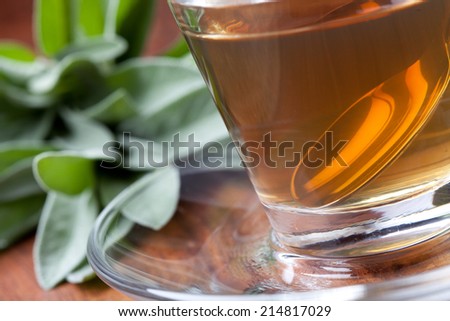 hot sage tea with silver spoon inside teacup, wooden floor, fresh bunch of sage in background, tilted
