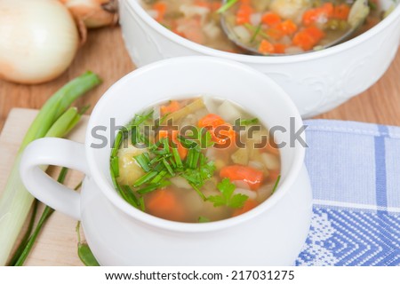 fresh vegetable soup in white bowl, herbs inside, big soup bowl in background, silver dipper inside, aerial view,