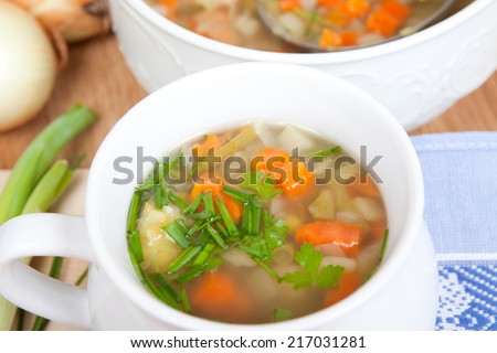 soup made of fresh vegetables, soup bowl in background with silver dipper inside, surrounded by different vegetables and dishware