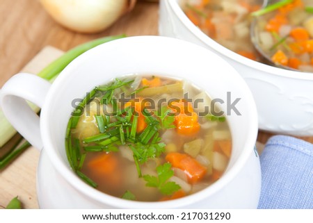 vegetable soup with fresh ingredients, in white bowl, big soup bowl with silver dipper in background, aerial view