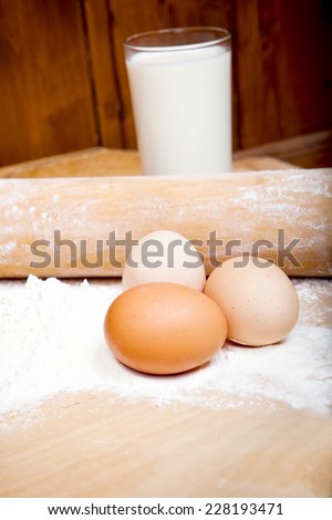 dough ingredients for baking, eggs, milk, flour, with rolling pin on old wooden noodle board,