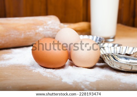 dough ingredients, eggs, milk, and flower, with wooden rolling pin and christmas cookie cutters
