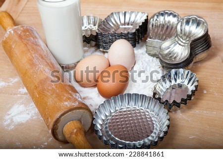 Ingredients for baking Christmas Cookies, with eggs, flour, milk, old wooden rolling pin and retro biscuit cutters,